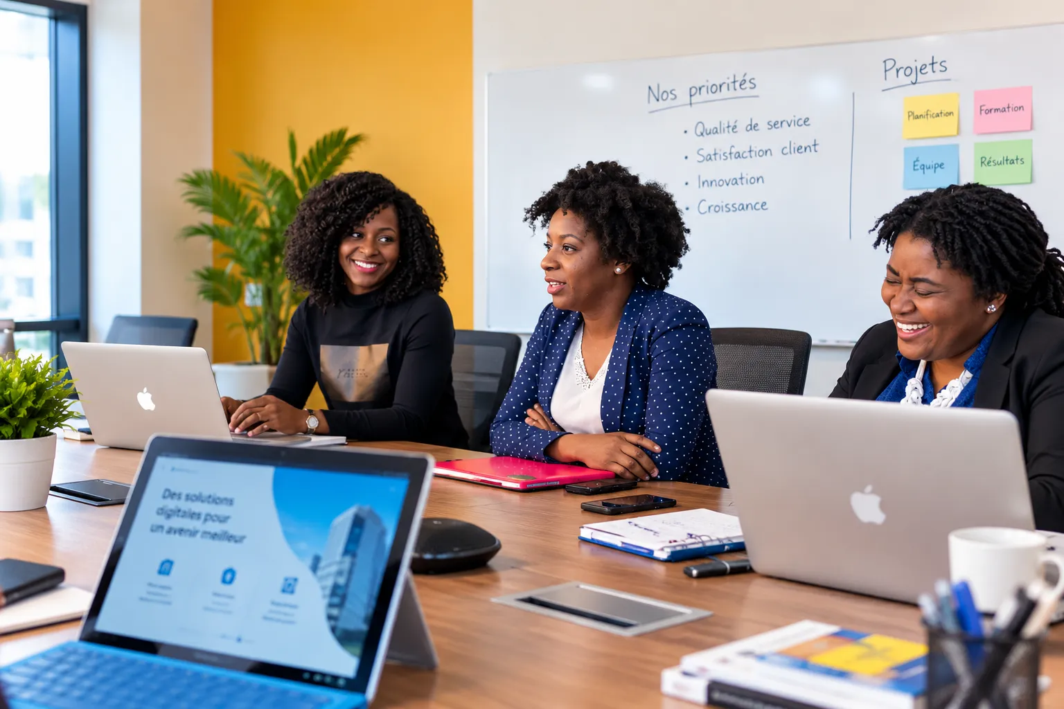 Trois collaboratrices souriantes en réunion devant un tableau « Nos priorités : qualité de service, satisfaction client, innovation, croissance »